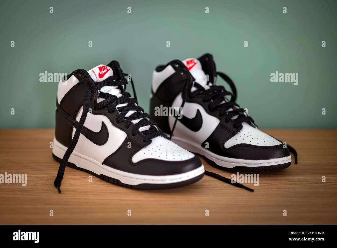 Schwarz-weiße Nike Dunk High Sneakers auf Holzregal mit hohem Design und rotem Nike Logo an der grünen Wand Stockfoto