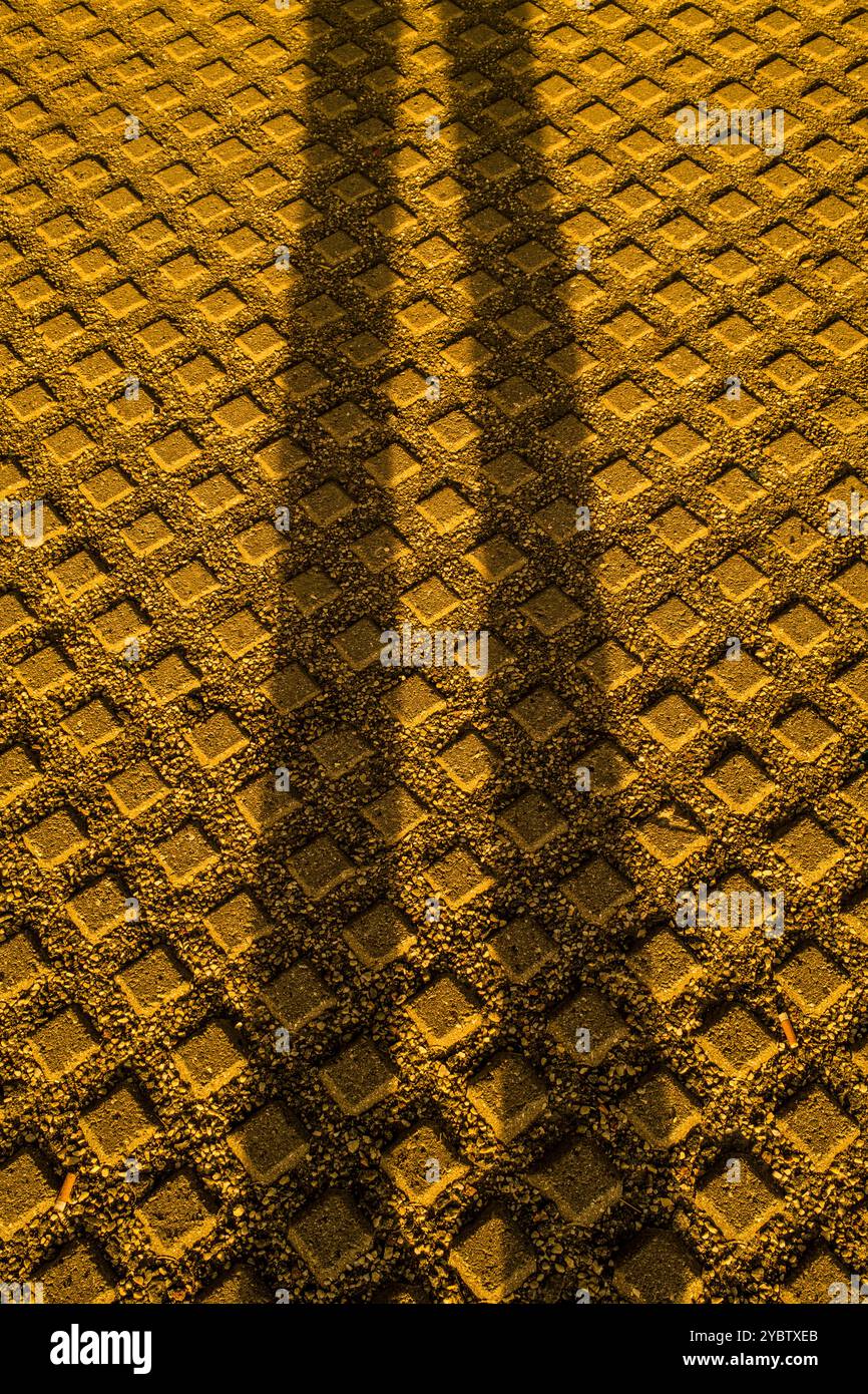 Das warme Leuchten des Sonnenuntergangs beleuchtet den Boden in Göteborg, während Schatten von einer nahegelegenen Brücke komplexe geometrische Muster auf der strukturierten Oberfläche erzeugen Stockfoto