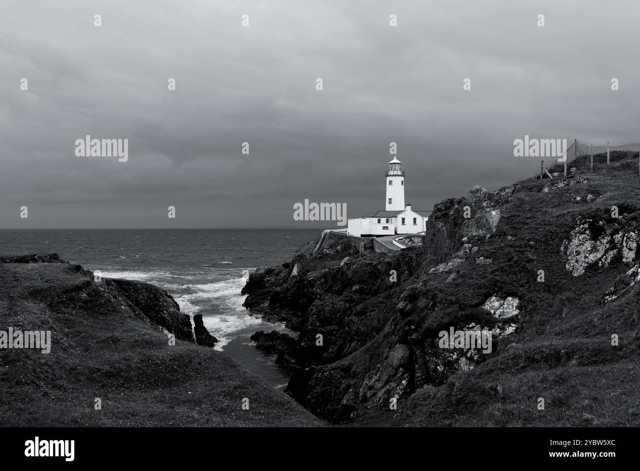 Ein einfarbiges Foto des Fanad Head Lighthouse während eines Sturms, das die scharfen Kontraste und Texturen des Meeres, der felsigen Klippen und des dunklen Clou hervorhebt Stockfoto