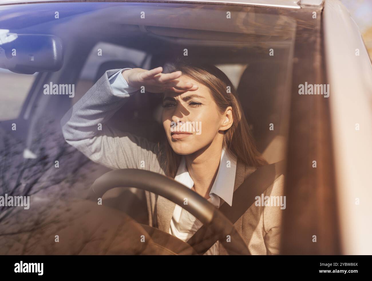 Hübsche junge Geschäftsfrau, die Auto fährt und Sonnenlichter direkt ins Gesicht und blinde Fahrer Stockfoto