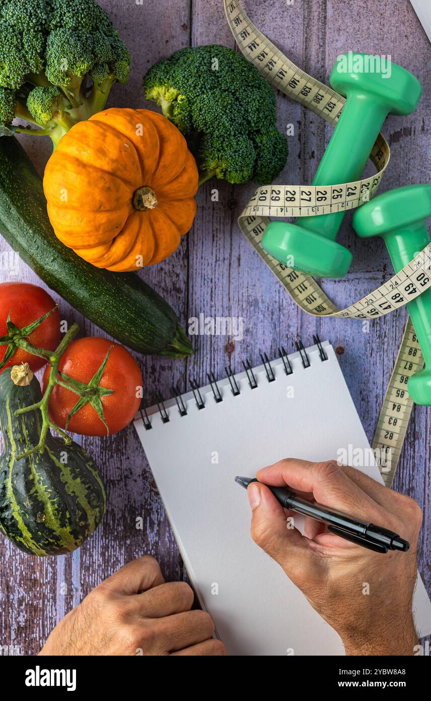 Frisches Gemüse, zwei Hände und ein Notizblock, Kurzhanteln und Maßband, Selbstverbesserungskonzept und Neujahrsvorsätze Stockfoto