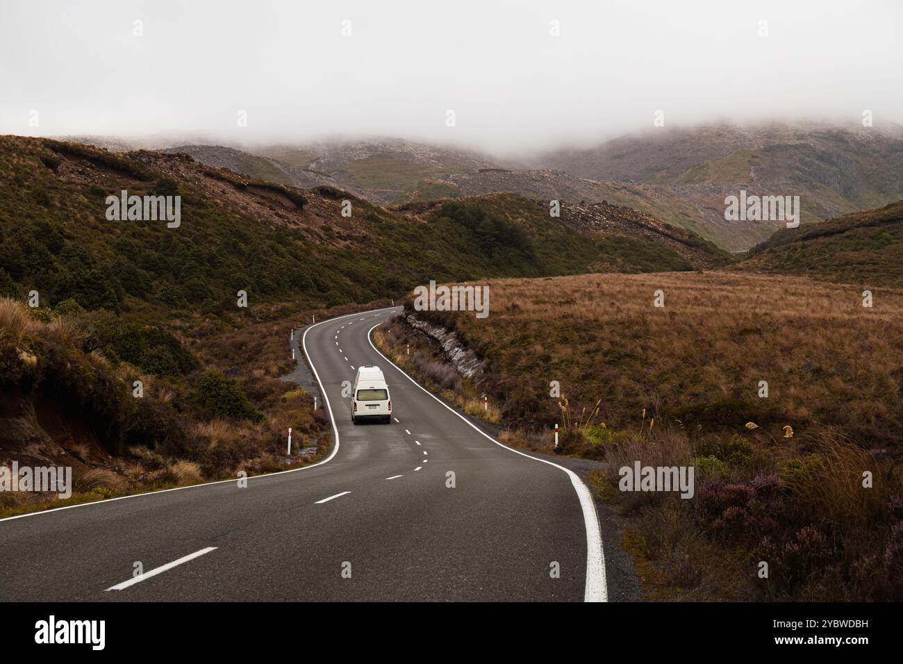 Weißer Wohnmobil fährt s-förmige Straße hinauf in Richtung nebeliger Bergkette im Tongariro-Nationalpark (Nordinsel, Neuseeland) Stockfoto