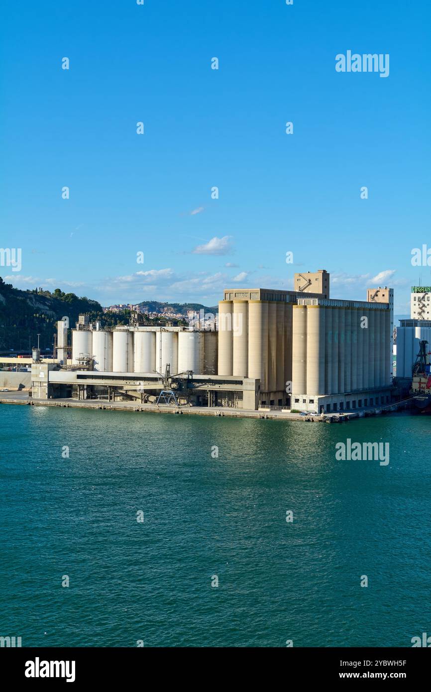 Barcelona. Espain - 20. Oktober 2024: Aus der Vogelperspektive auf den Industriehafen von Barcelona mit Getreidesillos unter blauem Himmel und ruhigem Meer. Stockfoto