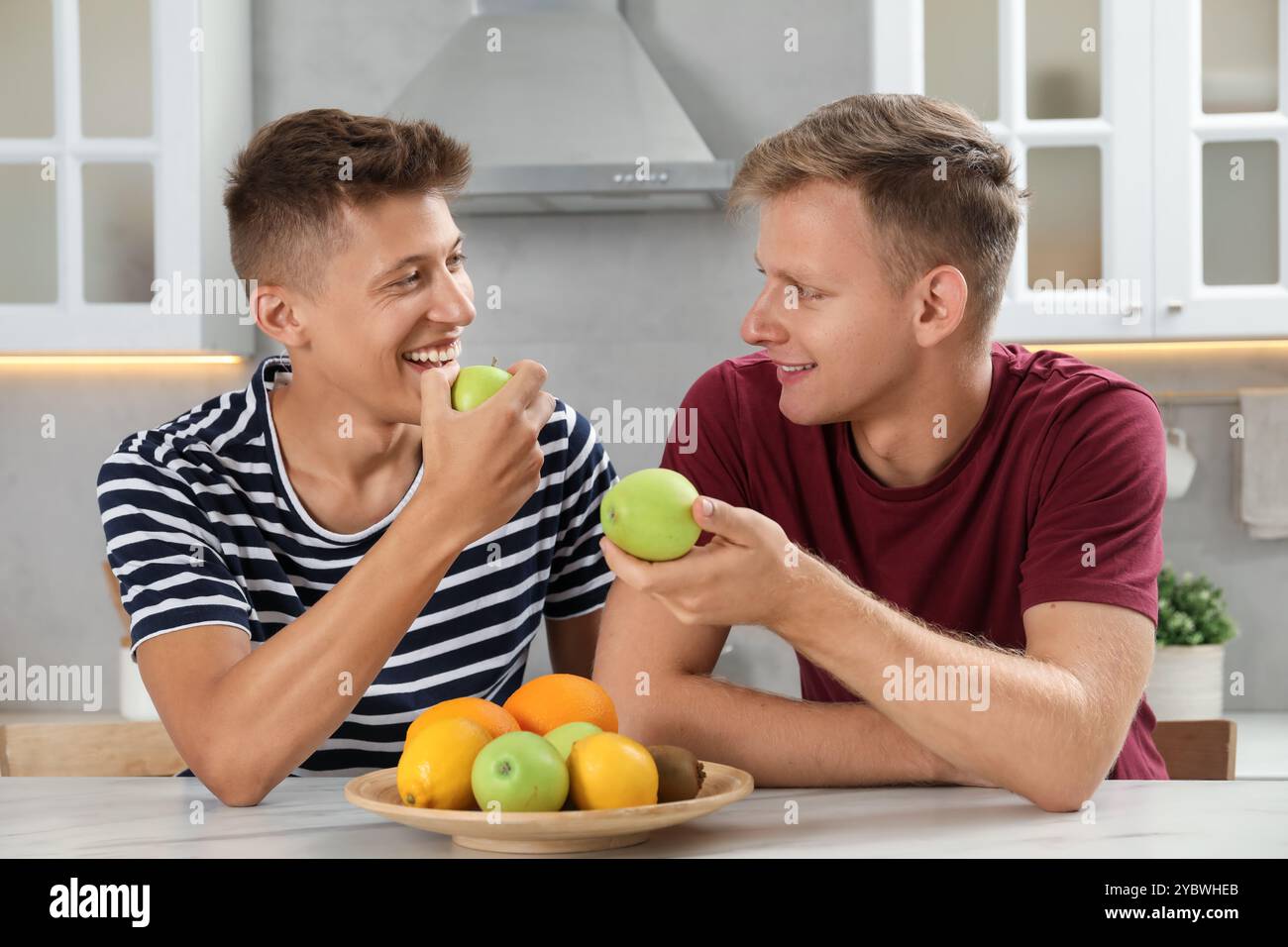 Glückliche Brüder essen Äpfel am Tisch in der Küche Stockfoto