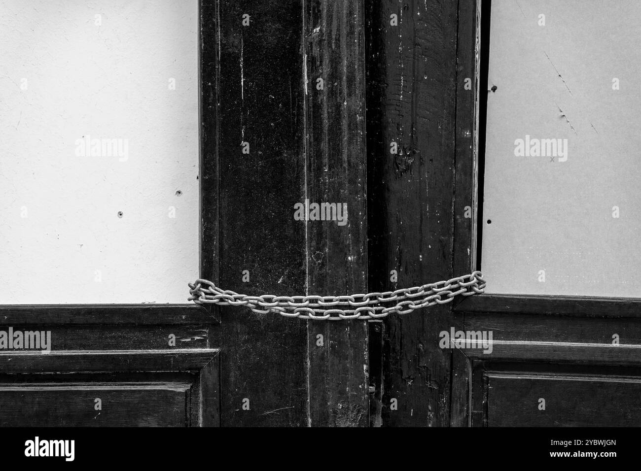 Geschäftsausfall: Geschlossener Holztürrahmen mit Kettenglied als Symbol für Schließung. Schwarz-weiß. Stockfoto