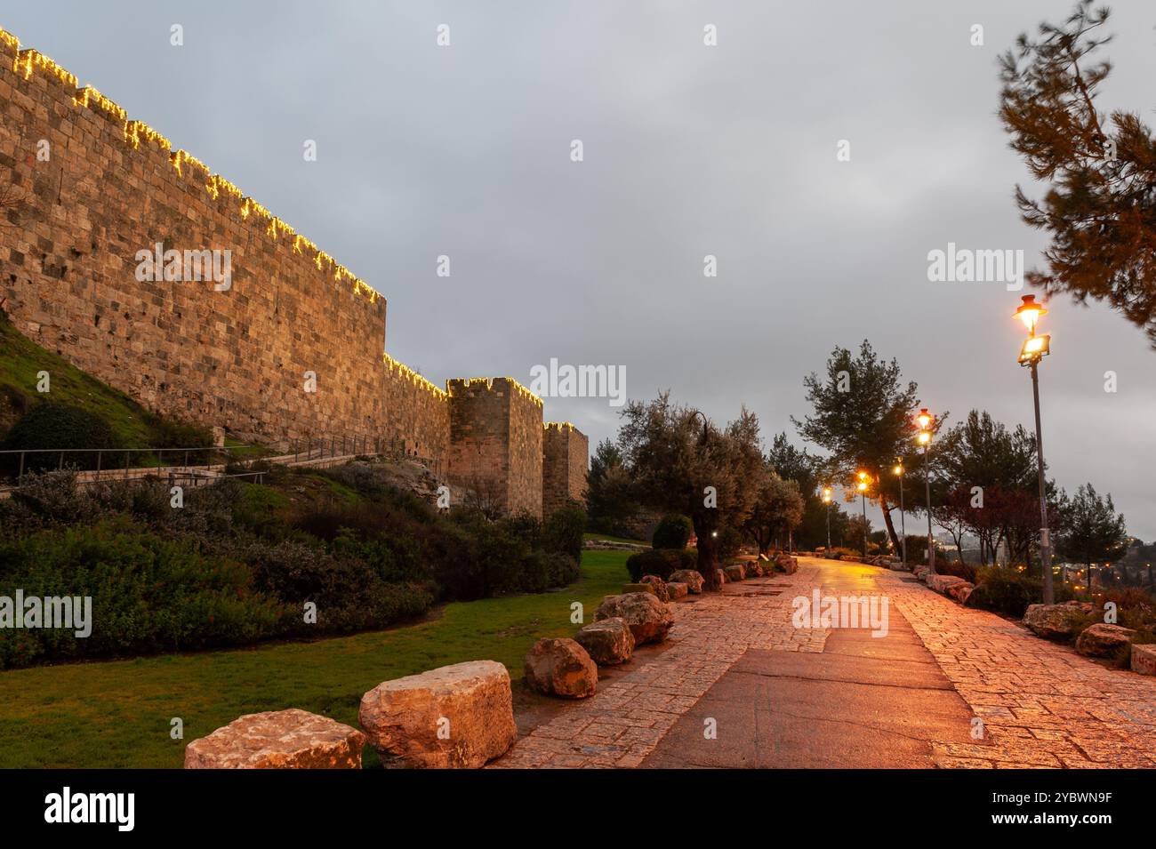 Ein Abschnitt der alten Steinmauern und Mauern der Altstadt von Jerusalem und der angrenzenden Straße, beleuchtet durch dekorative Lichter auf dem Mt. Zion. Stockfoto