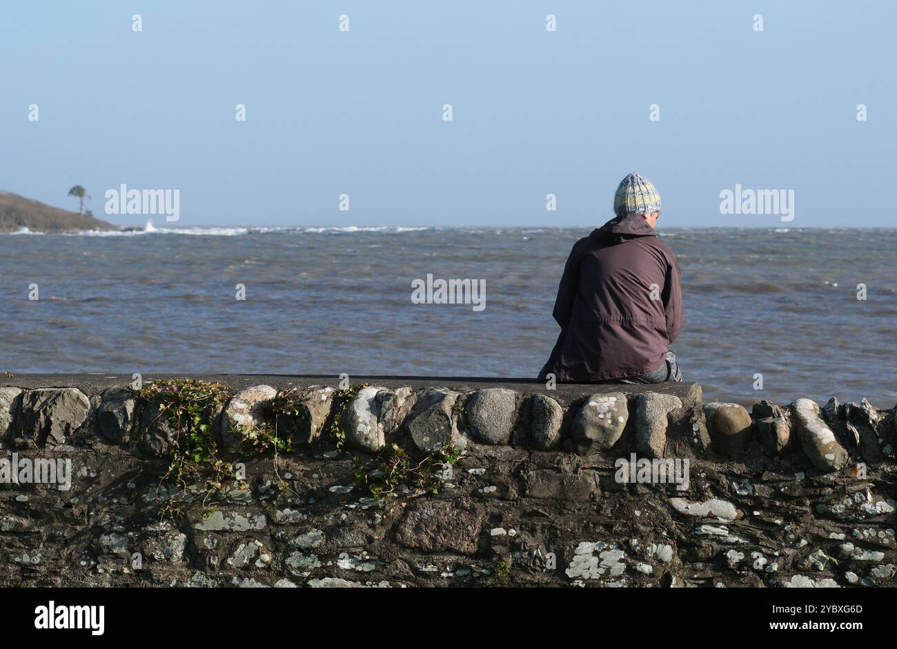 Eine Einzelperson saß im Herbst 2024 auf einer Meeresmauer und beobachtete das Meer - Schottland Großbritannien Stockfoto