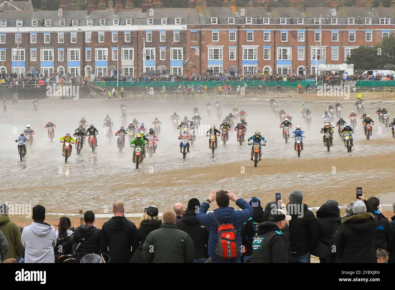 Weymouth, Dorset, Großbritannien. Oktober 2024. Mehr als 300 Fahrer, die von Tausenden von Zuschauern beobachtet werden, nehmen am 40. Motocross-Rennen in Weymouth Beach Teil, auf einem provisorischen Golfplatz, der von Baggern aus dem goldenen Sand des Resorts geschnitzt wurde. Die jährliche kostenlose Veranstaltung wird vom Purbeck Motocross Club veranstaltet. Die Fahrer laden mit hoher Geschwindigkeit bis zur ersten Kurve zu Beginn eines Rennens auf. Bildnachweis: Graham Hunt/Alamy Live News Stockfoto