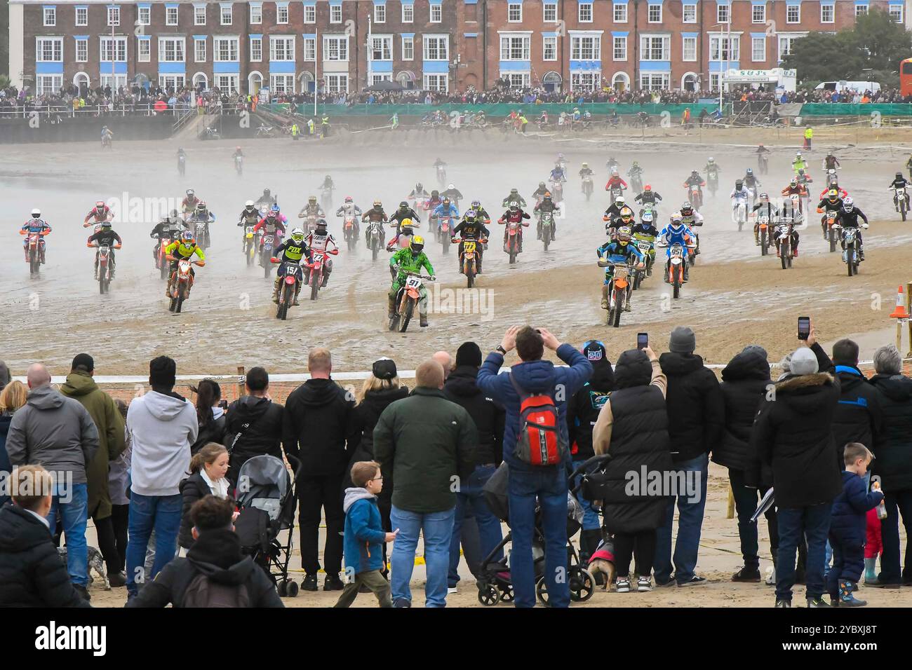 Weymouth, Dorset, Großbritannien. Oktober 2024. Mehr als 300 Fahrer, die von Tausenden von Zuschauern beobachtet werden, nehmen am 40. Motocross-Rennen in Weymouth Beach Teil, auf einem provisorischen Golfplatz, der von Baggern aus dem goldenen Sand des Resorts geschnitzt wurde. Die jährliche kostenlose Veranstaltung wird vom Purbeck Motocross Club veranstaltet. Die Fahrer laden mit hoher Geschwindigkeit bis zur ersten Kurve zu Beginn eines Rennens auf. Bildnachweis: Graham Hunt/Alamy Live News Stockfoto