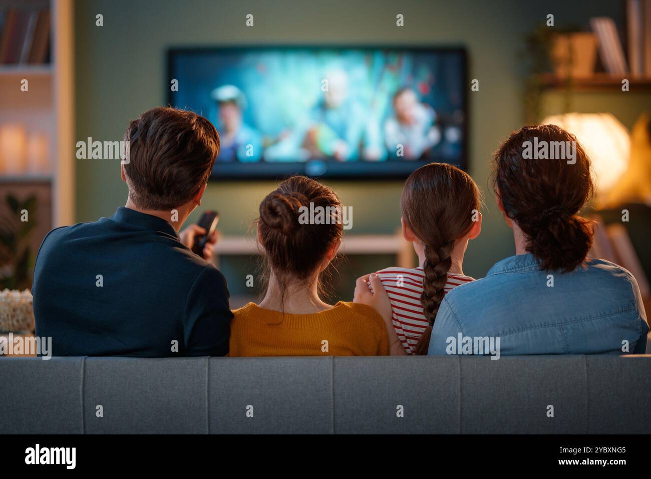 Glückliche Familie, die Zeit miteinander verbringt. Mutter, Vater und Kinder schauen fern, Filme mit Popcorn am Abend zu Hause. Stockfoto