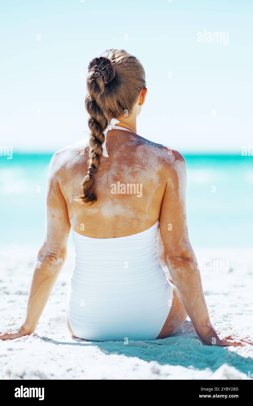Junge Frau im Badeanzug sitzt am Sandstrand. Rückansicht Stockfoto