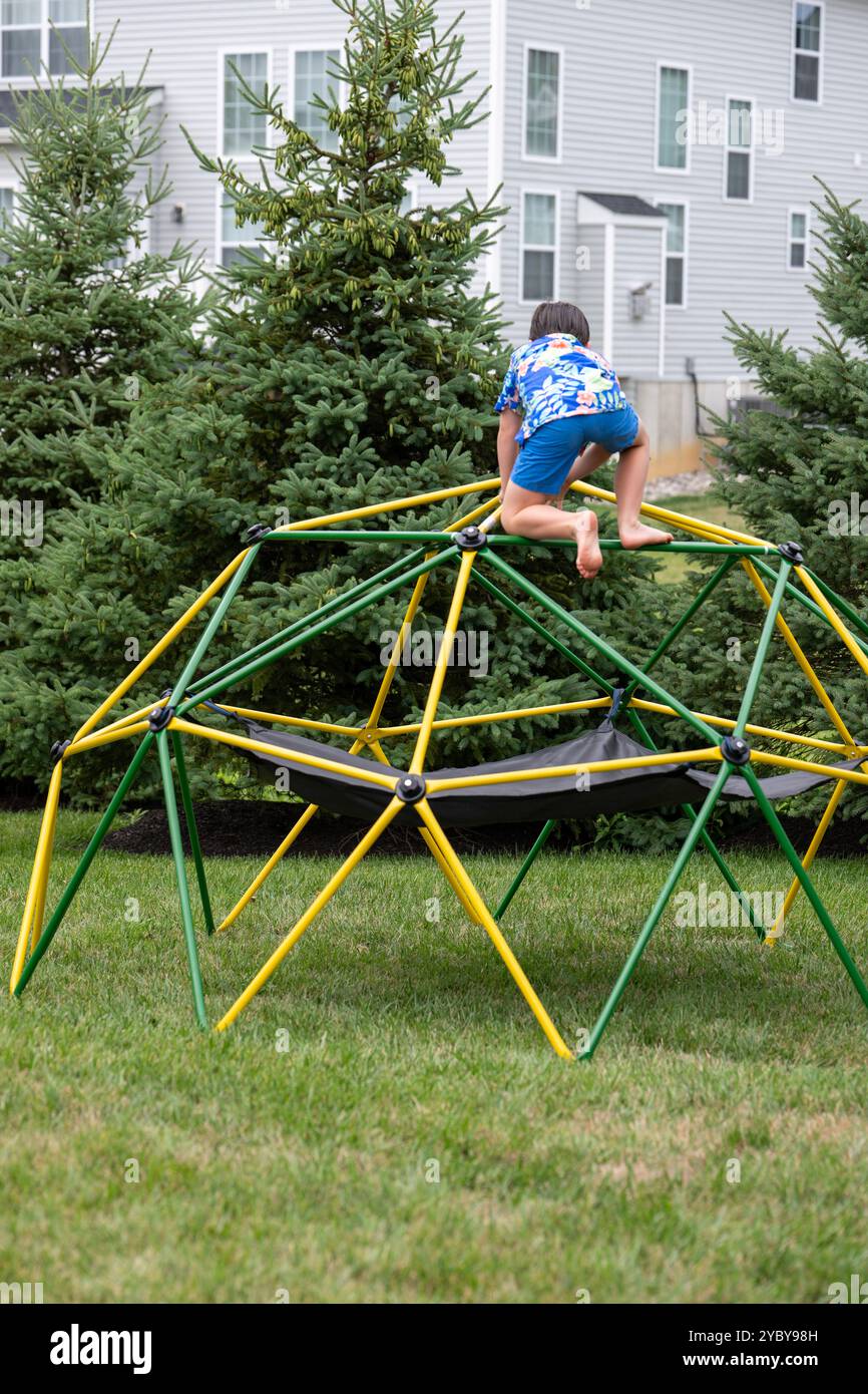 Ein achtjähriger Junge klettert auf eine geodätische Kletterstruktur in seinem Garten. Stockfoto