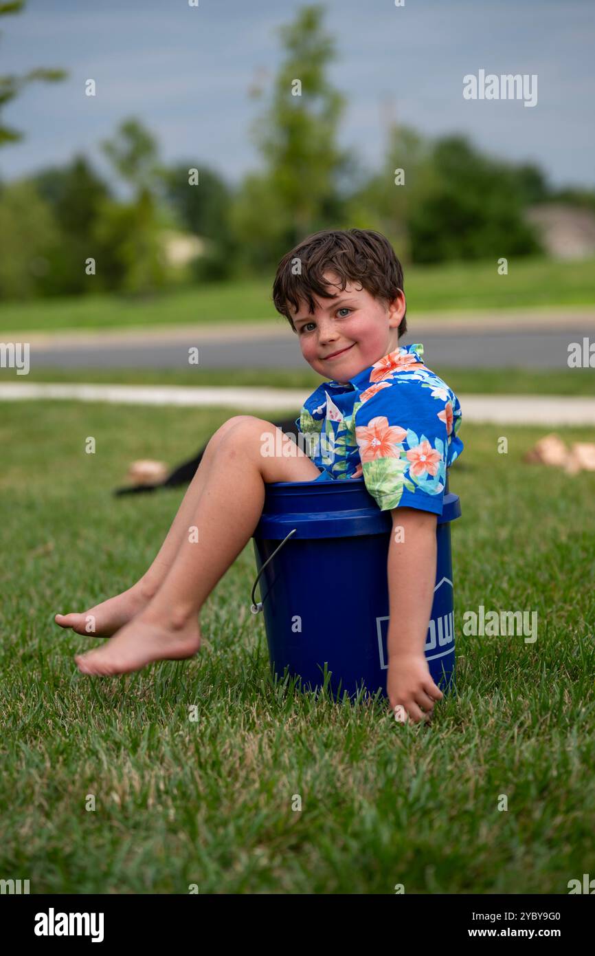 Ein achtjähriger Junge sitzt in einem blauen Eimer. Stockfoto