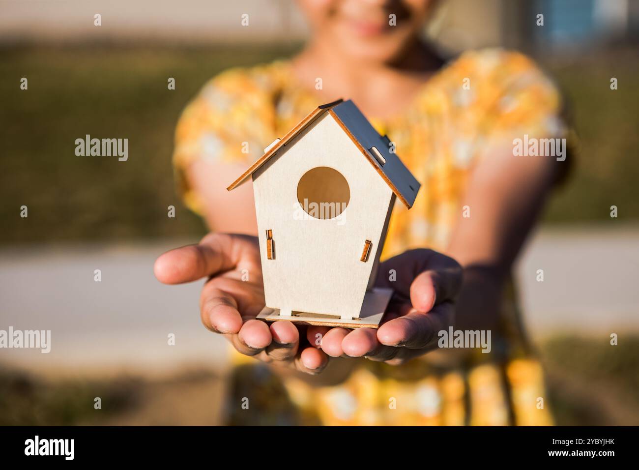 Kinderhände halten ein kleines weißes Miniaturspielhaus. Hypothekenversicherung Traumumzug und Immobilienkonzept Stockfoto