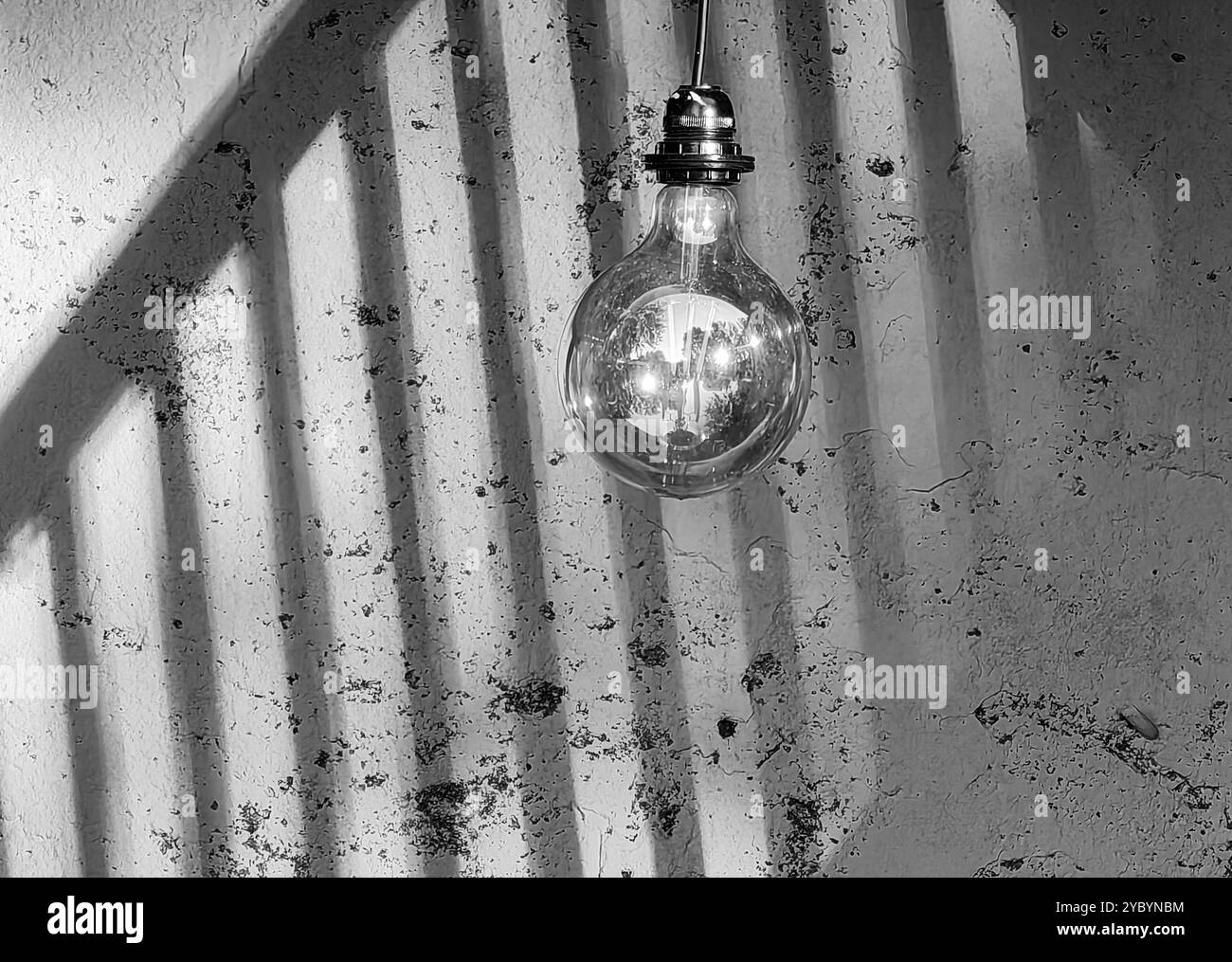 Be the Light in the Dark: Glühbirne gegen Schatten auf einer Wand mit Zaunhintergrund. Stockfoto