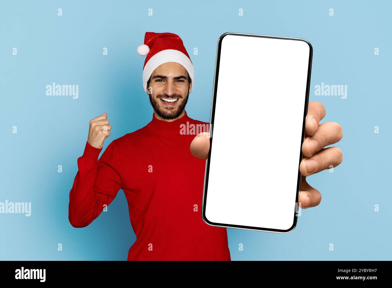 Fröhlicher Mann in einem Weihnachtsmütze zeigt Smartphone auf blauem Hintergrund Stockfoto