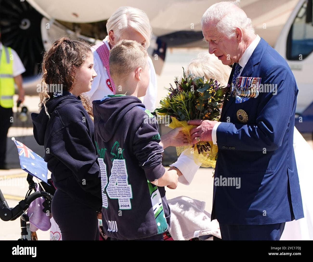 König Karl III. Spricht mit zwei Schülern, die Blumen für die offizielle australische Begrüßungsfeier am Flughafen Canberra am zweiten Tag ihres Besuchs in Australien und Samoa präsentieren. Bilddatum: Montag, 21. Oktober 2024. Stockfoto