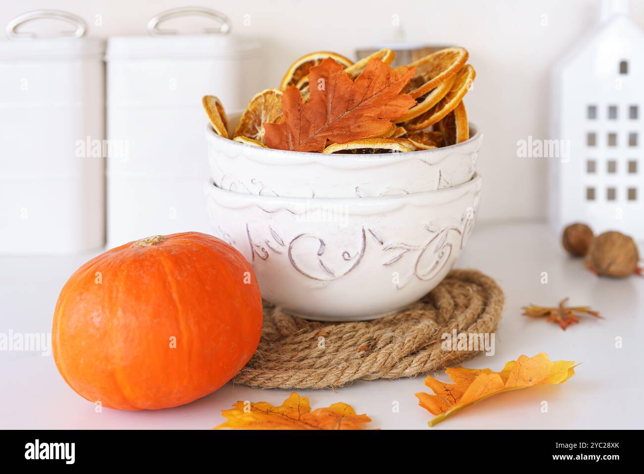 Weiße Schüssel gefüllt mit getrockneten Orangenscheiben, orangefarbenem Kürbis und bunten Herbstblättern auf dem Hintergrund in gemütlichem Kithen. Herbstdekor, wunderschöne Tablewa Stockfoto