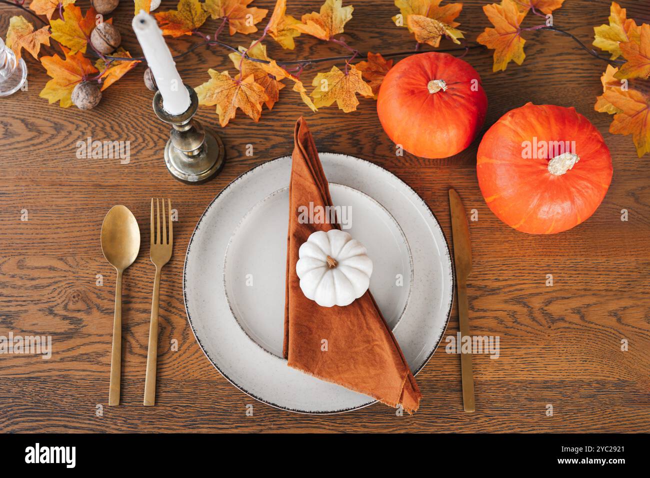 Esstisch in warmen Herbstfarben mit orangefarbenen Kürbissen, dekorativer Serviette und Besteck, umgeben von Herbstblättern und Kerzen. Tischeinstellung für Herbst h Stockfoto