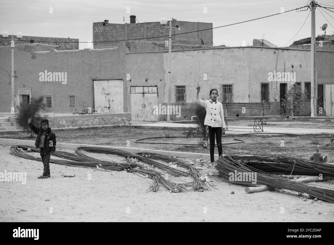 Schwarzweiß-Foto von zwei Kindern, die in der Kamera neben der Hauptstraße der Stadt winken. Es ist eine typische Tagesszene aus Marokko in der Nähe der Oase von Stockfoto