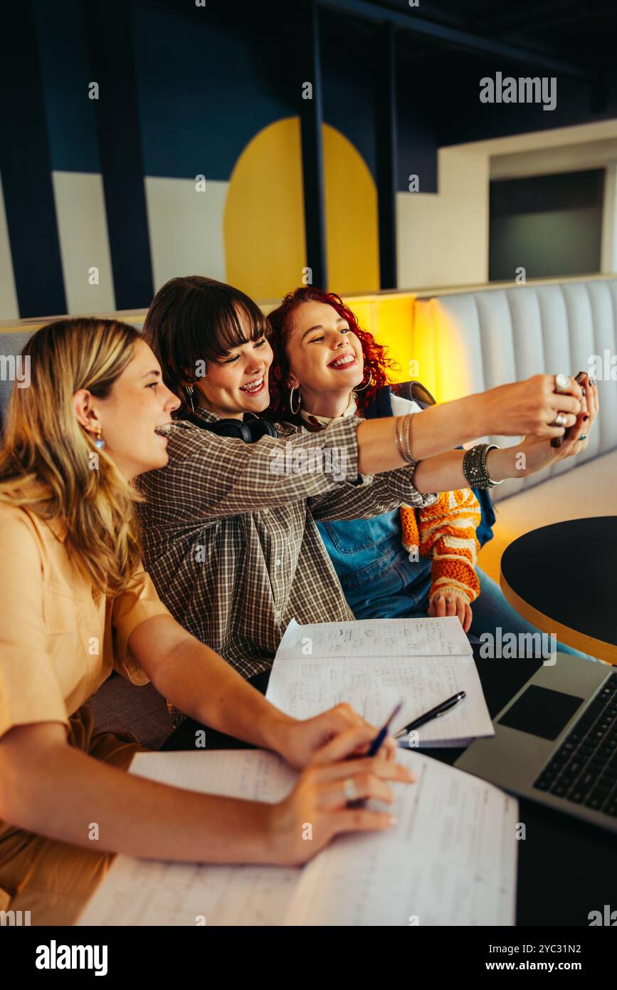 Freunde in einem freudigen Selfie-Moment während des Studiums in der Schule festgehalten. Die Gruppe sitzt mit Notizbüchern und einem Laptop, was Spaß und Geselligkeit widerspiegelt. Stockfoto