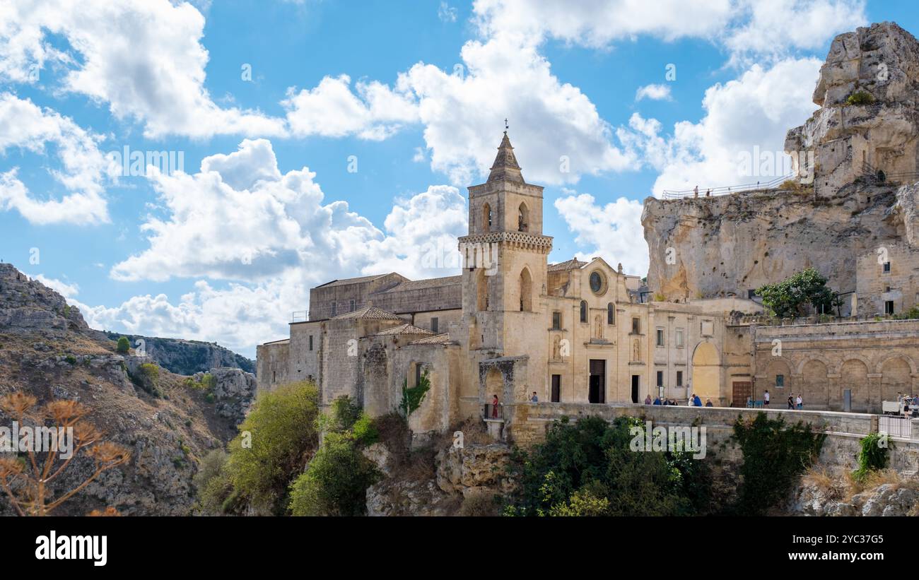 Im Herzen von Matera, Apulien, Italien, erheben sich die alten Steinbauten majestätisch, eingerahmt von einem strahlend blauen Himmel und geschwollenen Wolken. Die reiche Geschichte fügt sich nahtlos in die atemberaubende Landschaft ein. Stockfoto