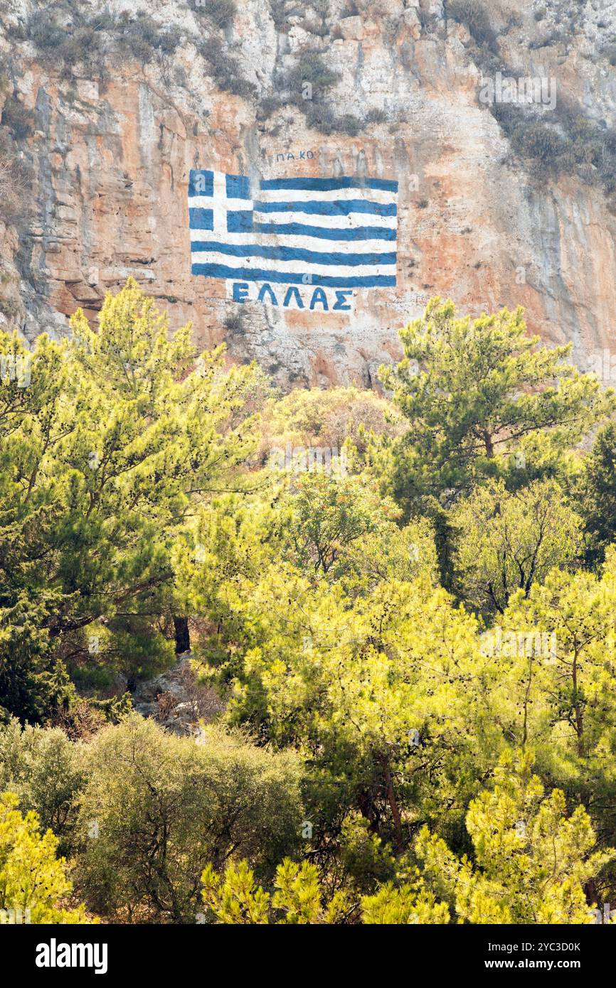 Eine griechische Flagge auf einer Klippe mit den Worten Griechenland in griechischem Alphabet, über der griechischen Insel Kastellorizo oder Meis in Griechenland, Europa Stockfoto