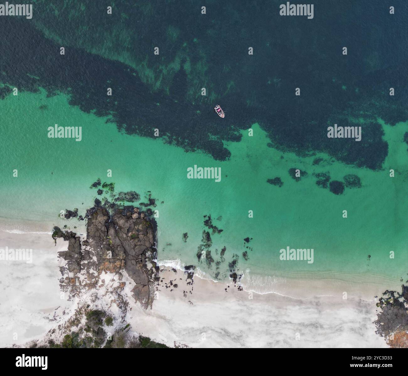 Blick aus der Vogelperspektive auf türkisfarbenes Wasser, weißen Sandstrand und kleines Boot Stockfoto