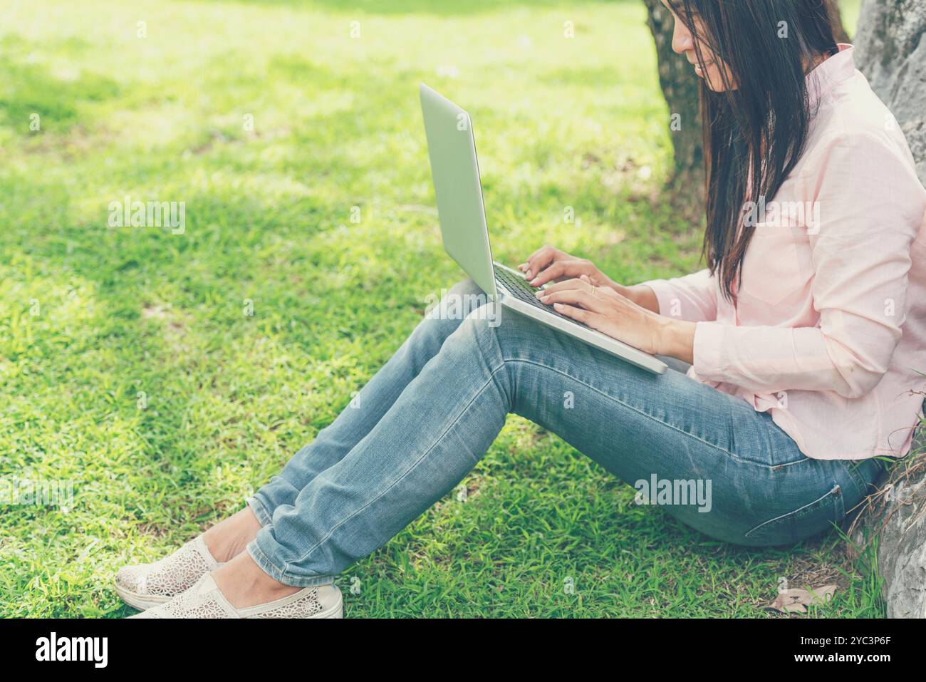 Asiatische Frau, die im grünen Park sitzt und einen Laptop benutzt. Frau, die an einem Laptop arbeitet, glückliches Unternehmerunternehmen, das ein Notebook verwendet, während die Hände auf der Tastatur tippen Stockfoto