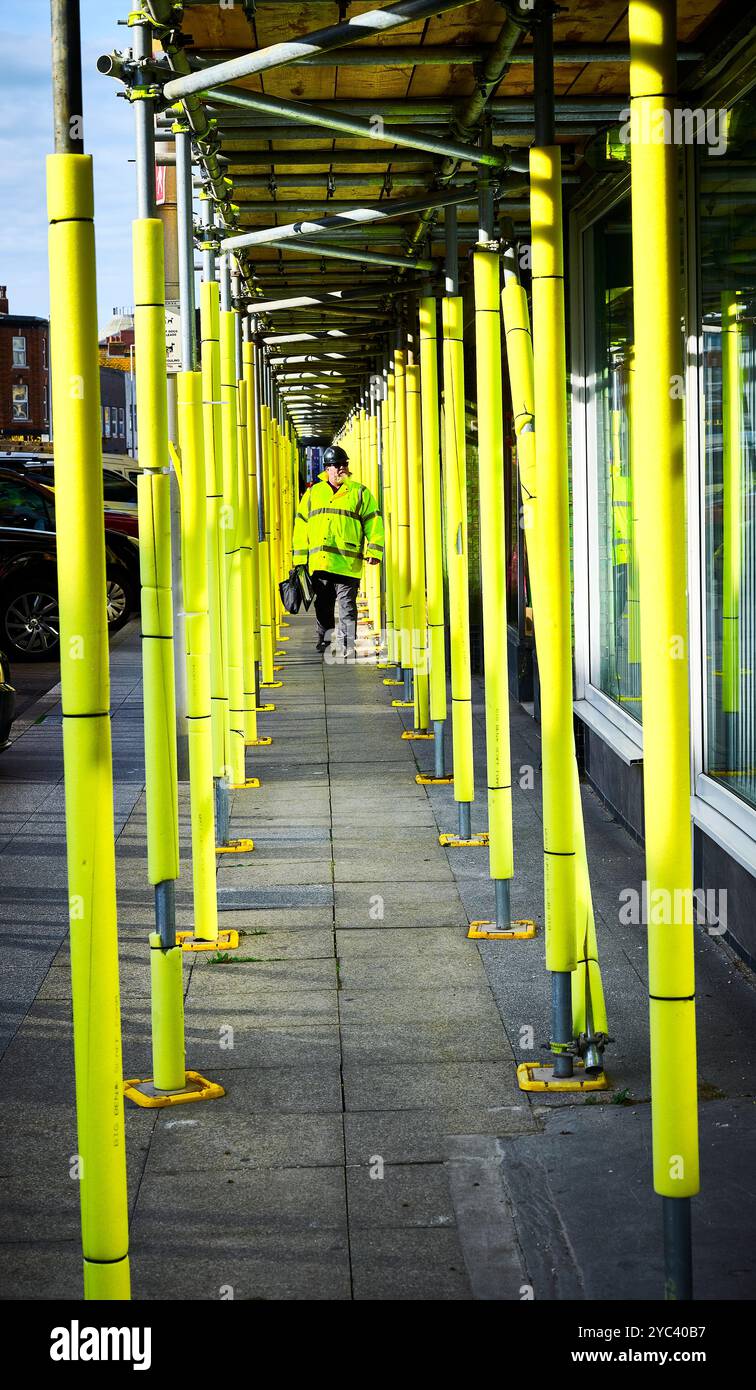 Mann in gut sichtbarem Mantel, der zwischen Gerüststangen mit gelbem Schaum umwickelt ist Stockfoto