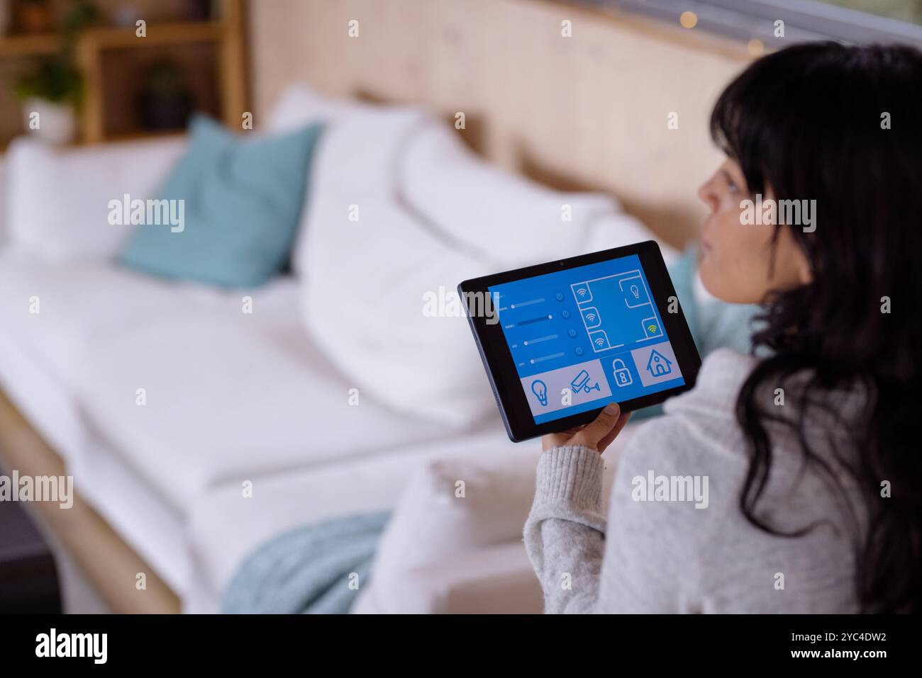 Frau, die ein Tablet zur Steuerung von Smart-Home-Geräten in einem gemütlichen Wohnzimmer verwendet Stockfoto