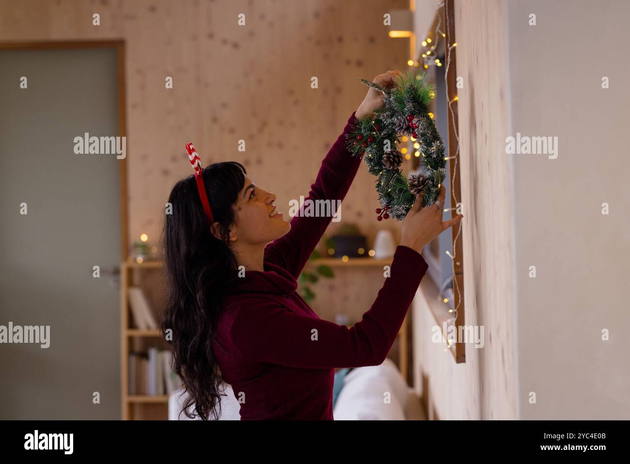 Frau, die das Haus mit Weihnachtskranz dekoriert, lächelt und feiert Stockfoto