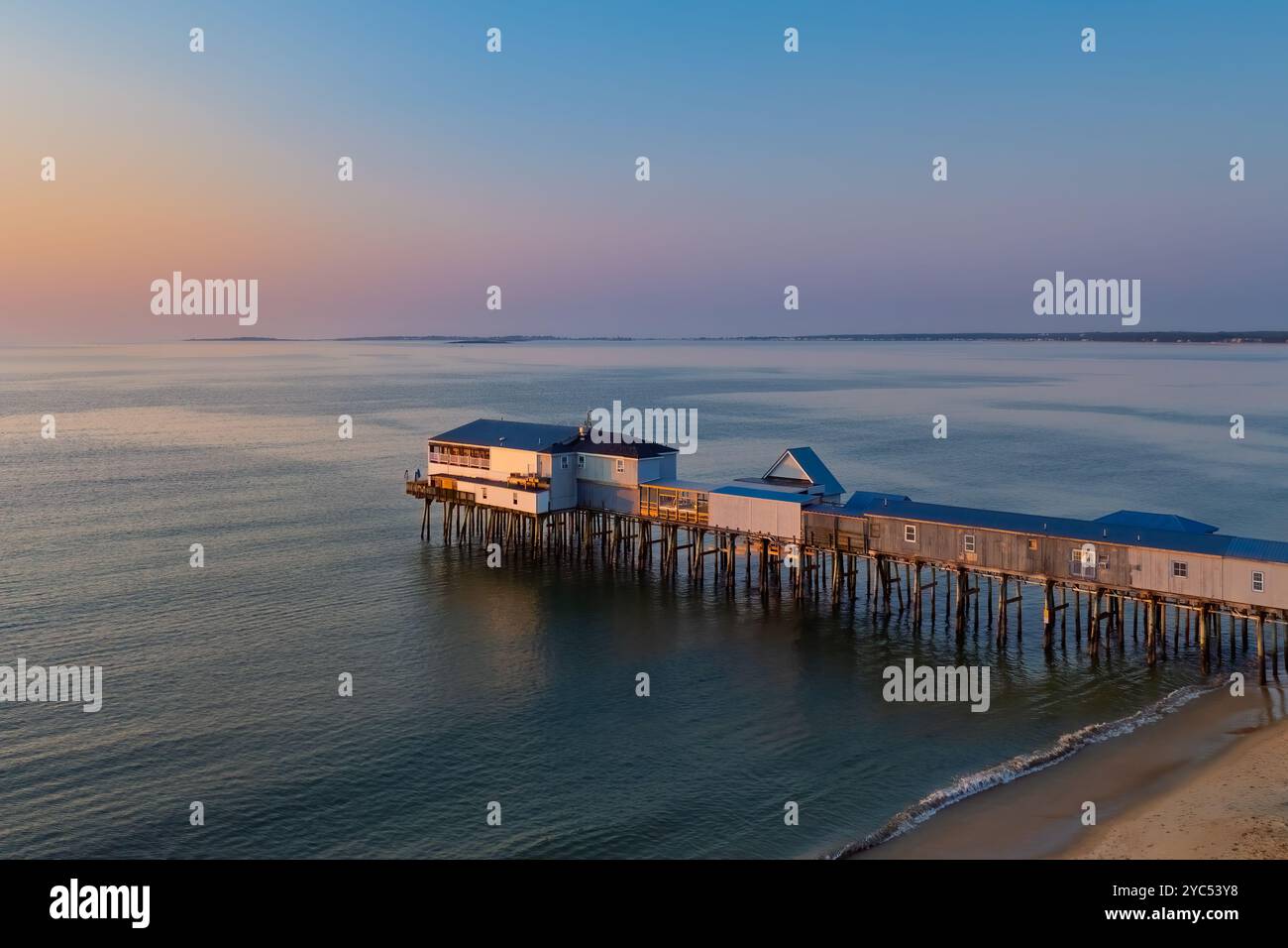 Sonnenlicht filtert durch die hölzernen Stützen eines Piers und wirft Reflexionen auf den nassen Sand darunter. Die ruhige Meereskulisse verstärkt den friedlichen geldautomaten Stockfoto