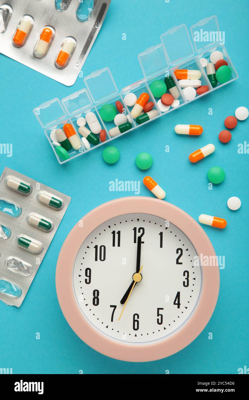 Weißer Wecker, Tablets und wöchentlicher Tablet-Organizer auf blauem Hintergrund. Zeitkonzept der Einnahme der Pillen. Draufsicht Stockfoto