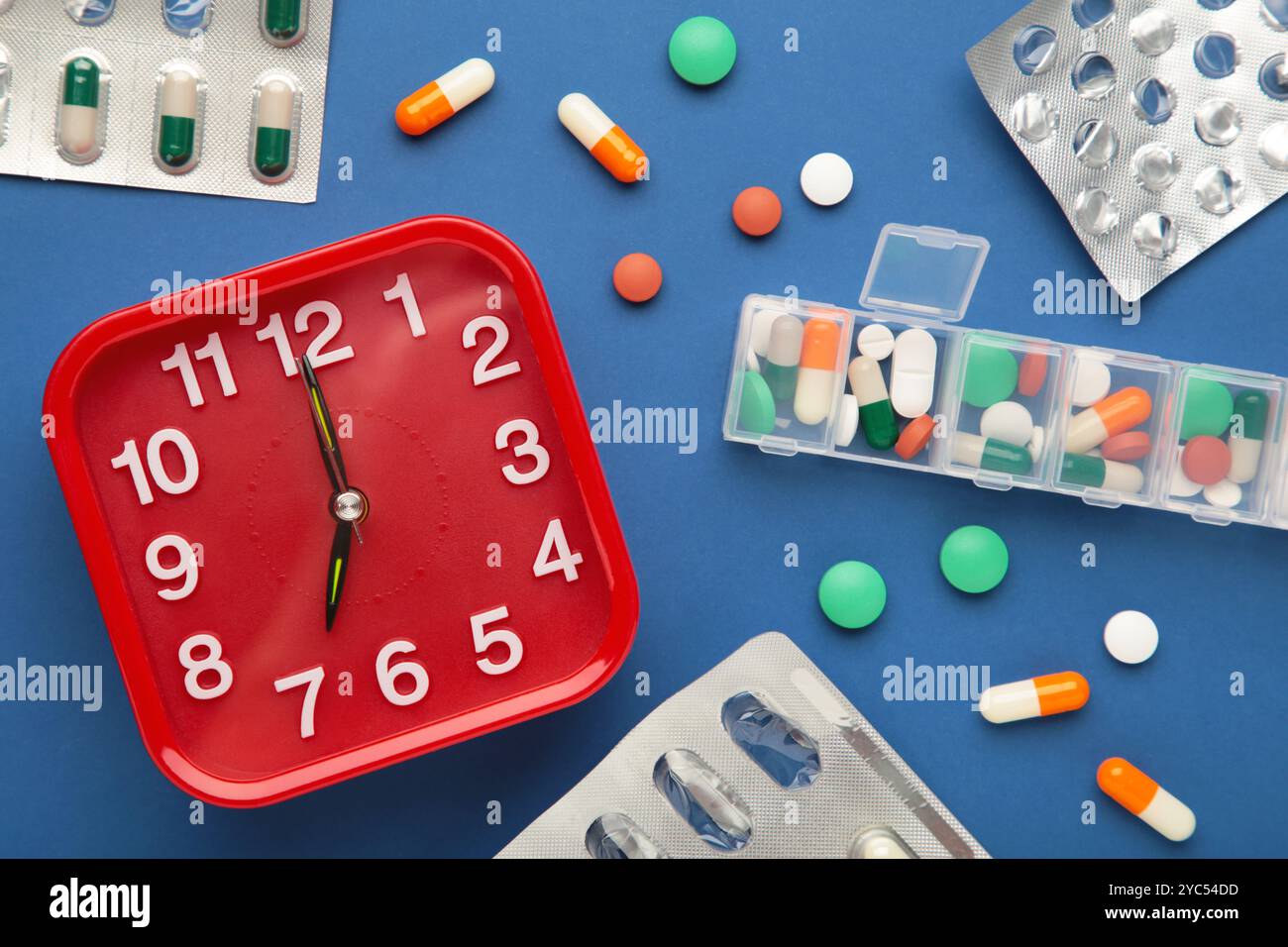 Weißer Wecker, Tablets und wöchentlicher Tablet-Organizer auf dunkelblauem Hintergrund. Zeitkonzept der Einnahme der Pillen. Draufsicht Stockfoto