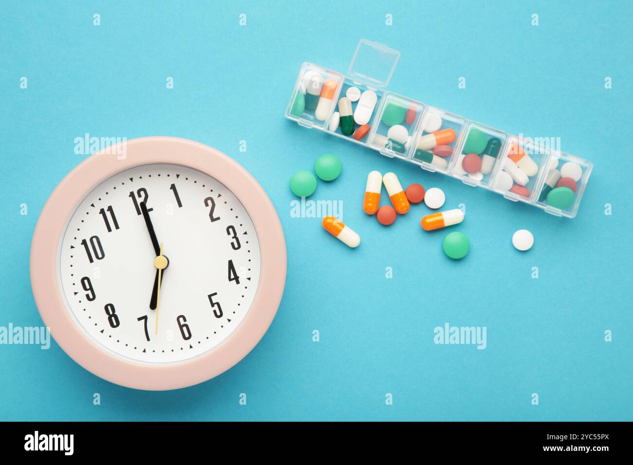 Rosafarbene Uhr, Tablets und wöchentlicher Tablettenordner auf blauem Hintergrund. Zeitkonzept der Einnahme der Pillen. Draufsicht Stockfoto