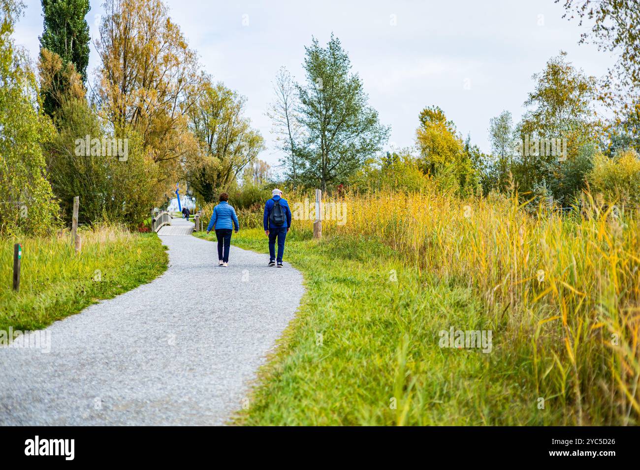 Ein Mann läuft in einem Park mit Bäumen und einem See im Hintergrund. Eine Frau läuft hinter ihm Stockfoto