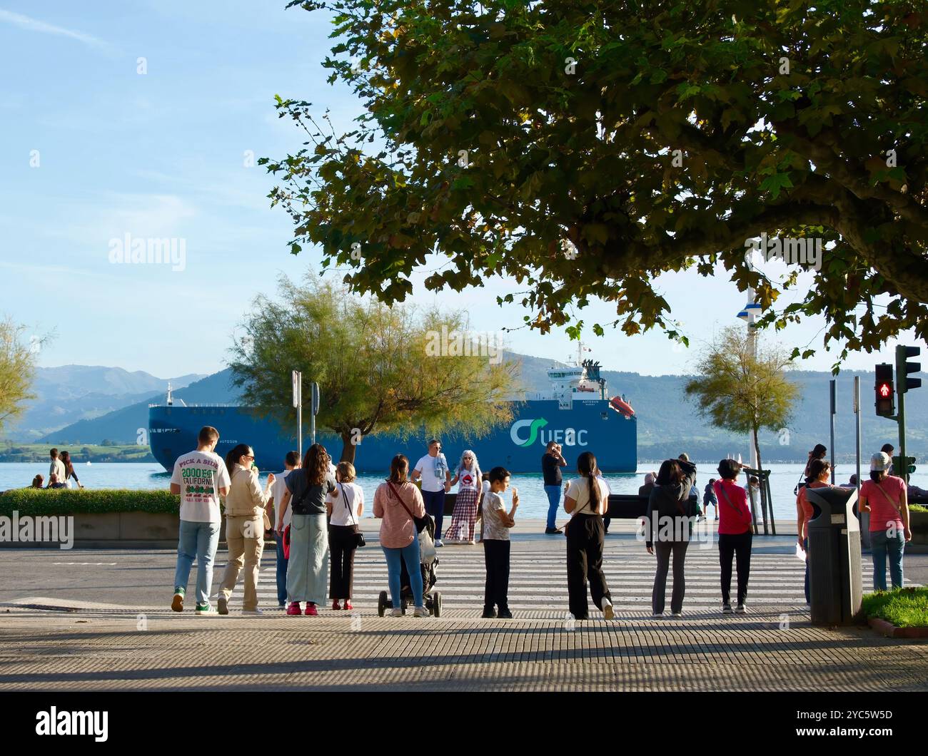 Menschen, die an der Ampel auf die Straße warten, während das Autosun-Frachtschiff den Hafen in der Bucht von Santander Cantabria Spanien verlässt Stockfoto