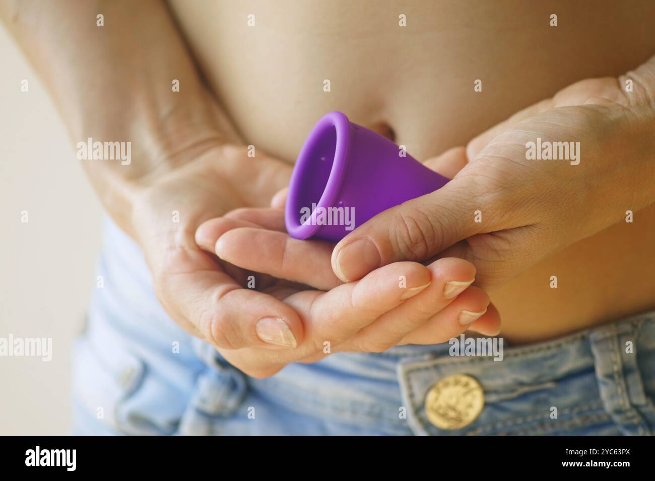 Nahaufnahme der Handflächen der Frau mit neuem violetten Menstruationstasse. Umweltbewusste Frau entscheidet sich für umweltfreundliche Menstruationshygieneprodukte Stockfoto