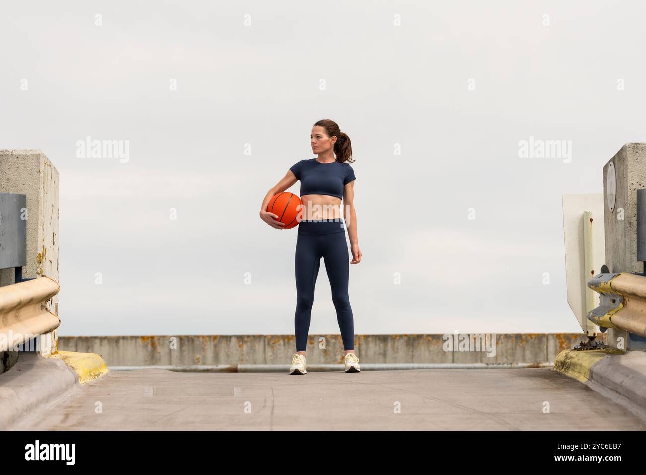 Sportliche Frau, die draußen einen Basketball unter dem Arm hält. Stockfoto