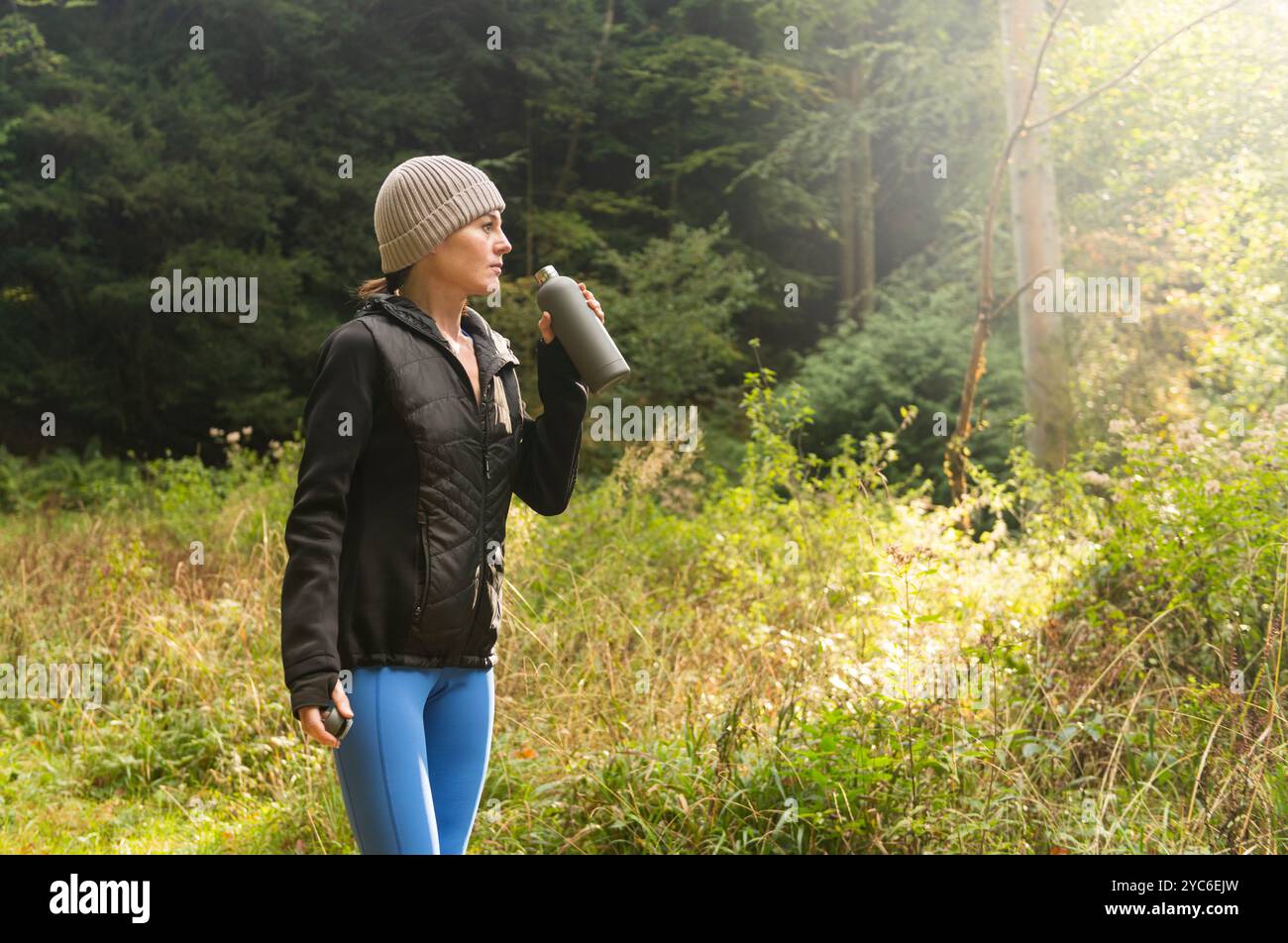 Sportliche Frau, die nach dem Training und Joggen im Freien in der herbstlichen Landschaft Wasser aus einer Flasche trinkt Stockfoto