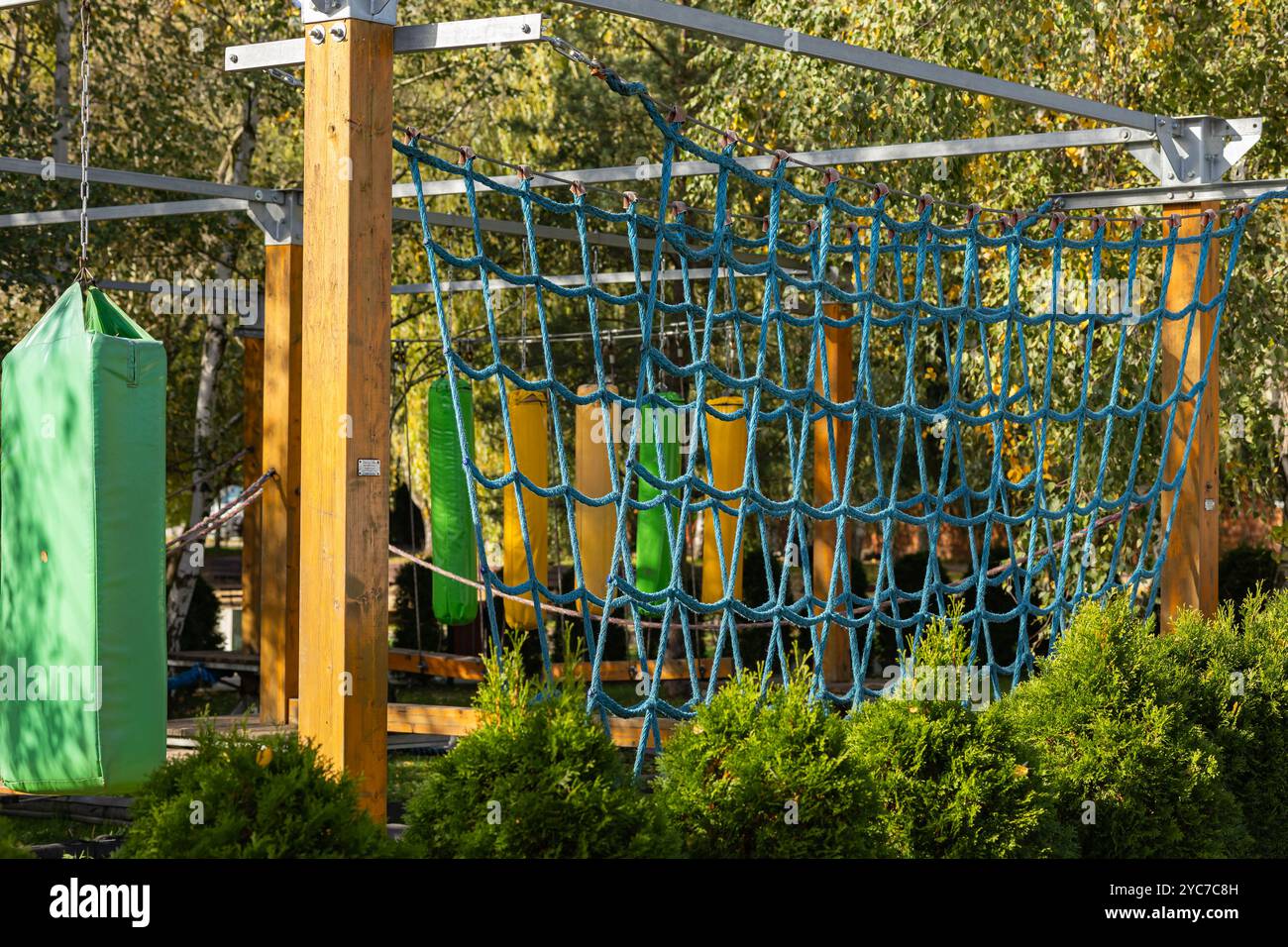 Farbenfroher Seilgarten im Freien mit Netz und Boxsäcken an sonnigen Herbsttagen. Konzept von Abenteuerspielplatz, aktivem Lifestyle und Sportausrüstung Stockfoto