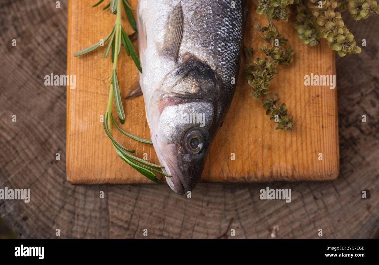 Roher Seebarsch auf Holztisch mit Kräutern und Gewürzen Stockfoto