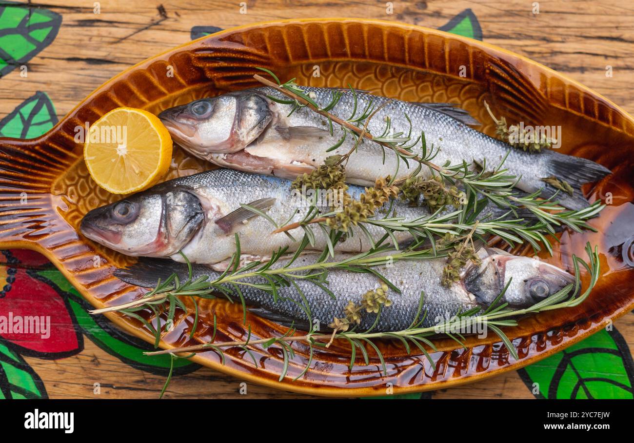 Roher Seebarsch auf Holztisch mit Kräutern und Gewürzen Stockfoto