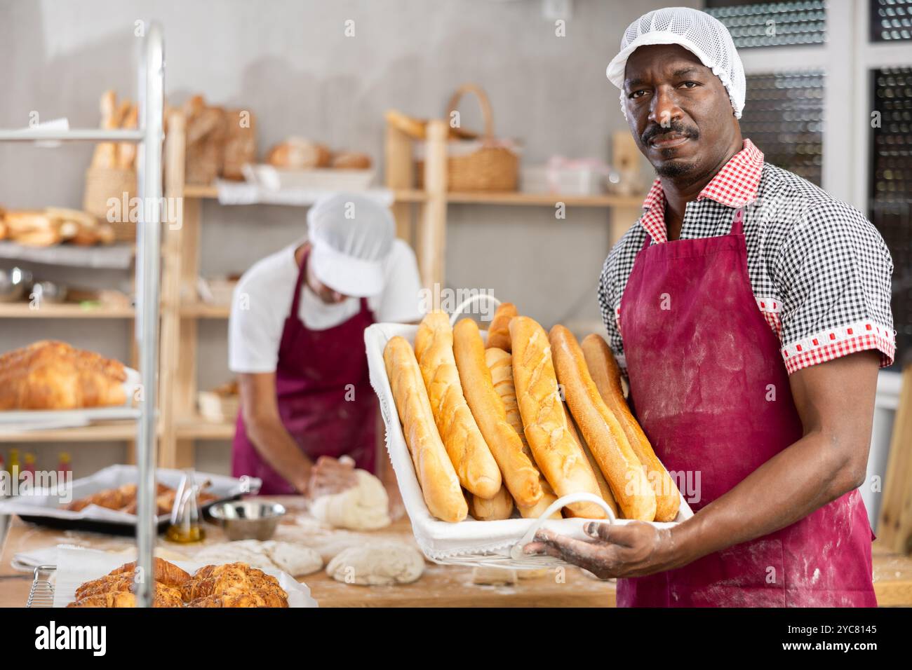 Erfolgreicher afrikanischer Bäcker, der frisch gebackene Baguettes hält Stockfoto