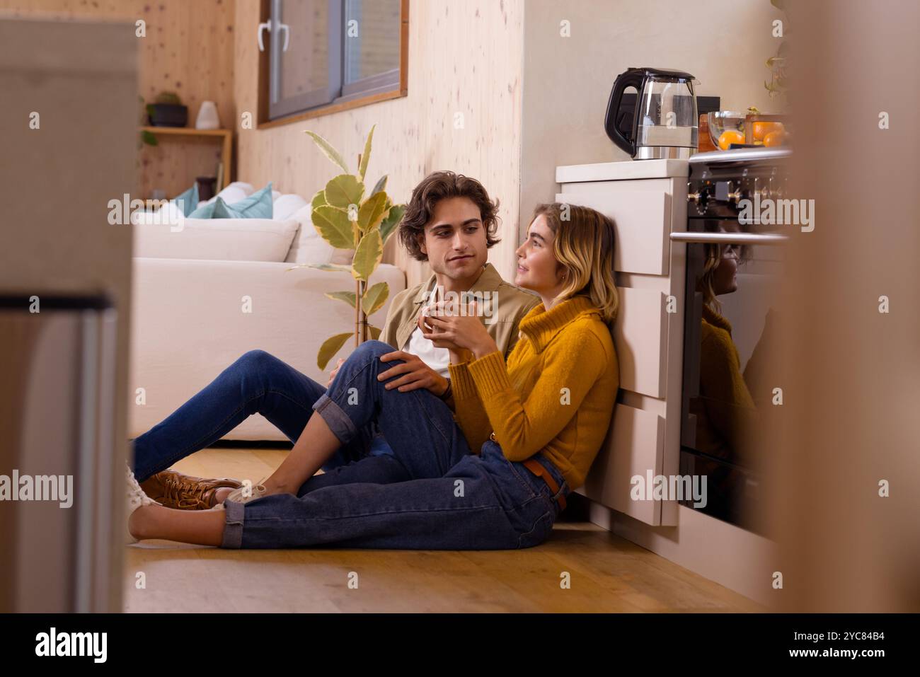 Paare sitzen auf dem Küchenboden und genießen warme Getränke und gemütliche Gespräche zu Hause Stockfoto