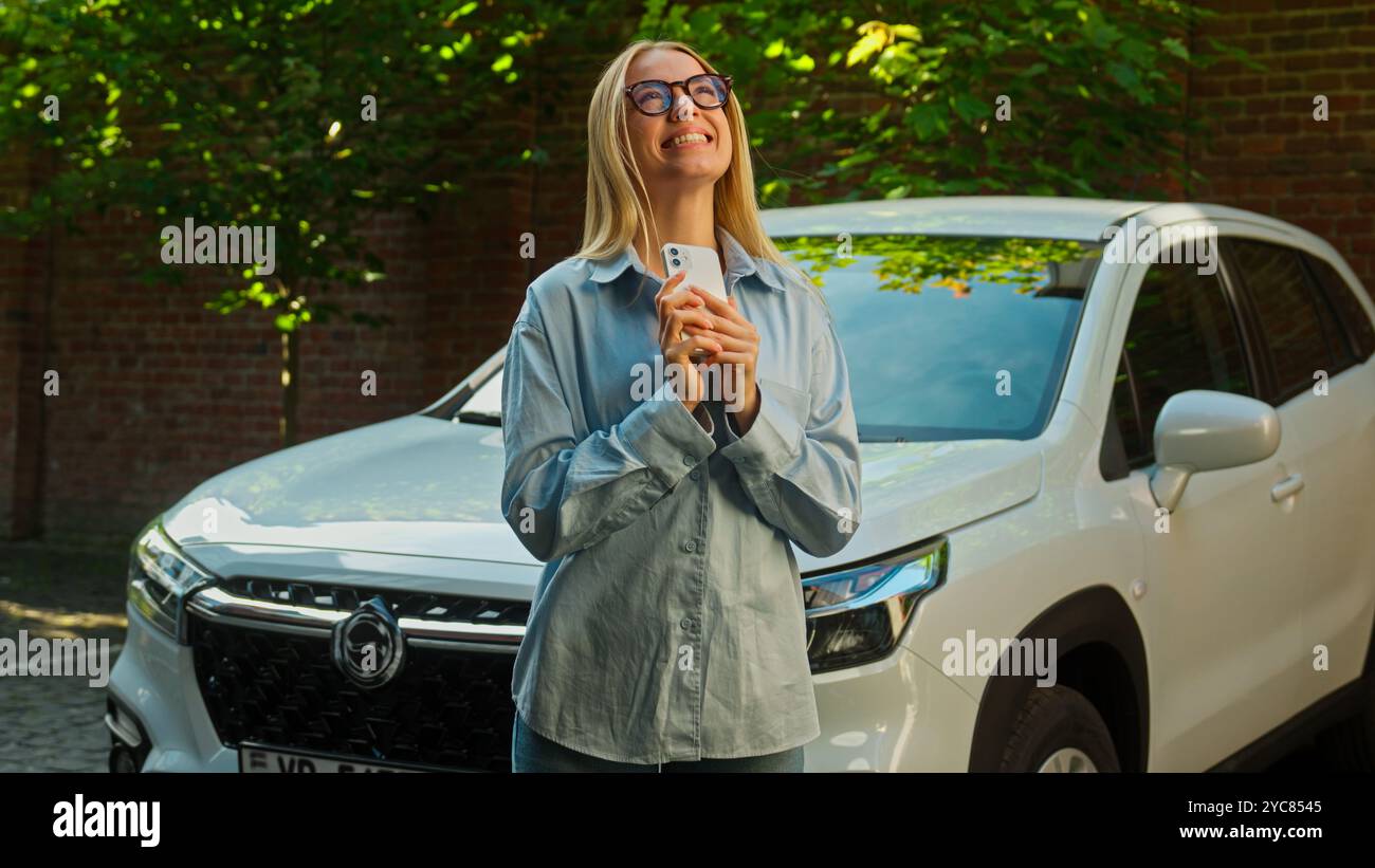 Glückliche kaukasische Frau mit Handy Smartphone gewinnen Kauf neues Auto Luxus Auto aufgeregt emotionale Freude Gadget Technologie Nachricht weiblichen Sieg Stockfoto