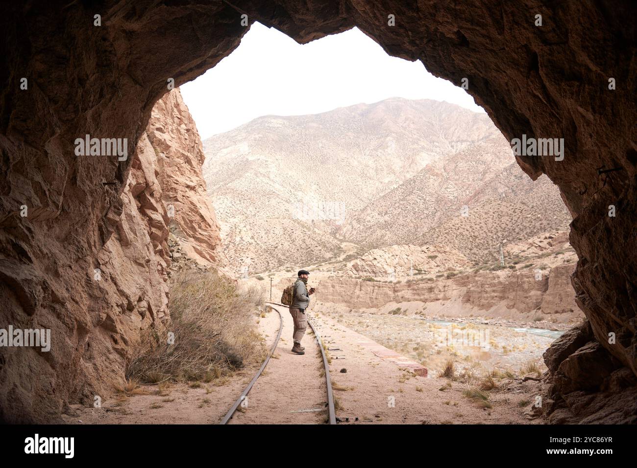 Ausgang eines Zugtunnels, draußen läuft eine Person entlang des Gleises. Im Hintergrund eine Berglandschaft. Stockfoto
