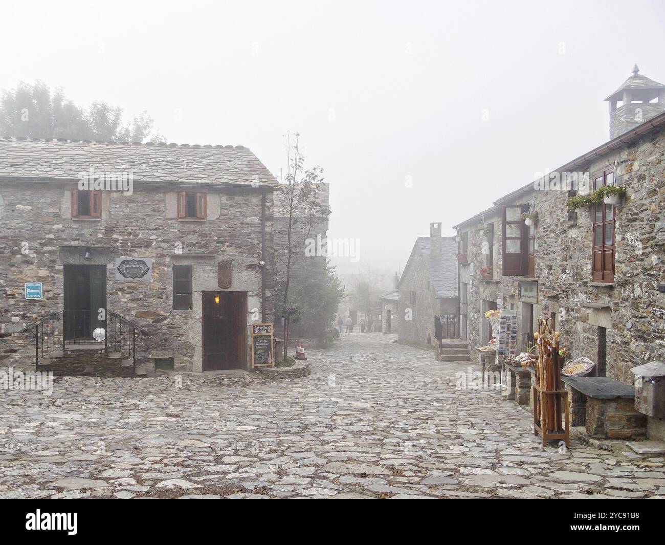 Geschäfte, Bars und Restaurants in einer nebeligen Kopfsteinpflasterstraße, O'Cebreiro, Galicien, Spanien, Europa Stockfoto