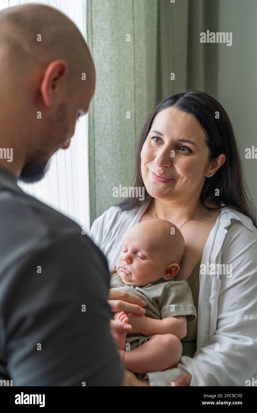 Familie mit neugeborenem Jungen. Eltern berühren sanft Baby und einander. Das Baby liegt leise in den Armen. Wärme und Harmonie in der Familie. Pflege und Stockfoto